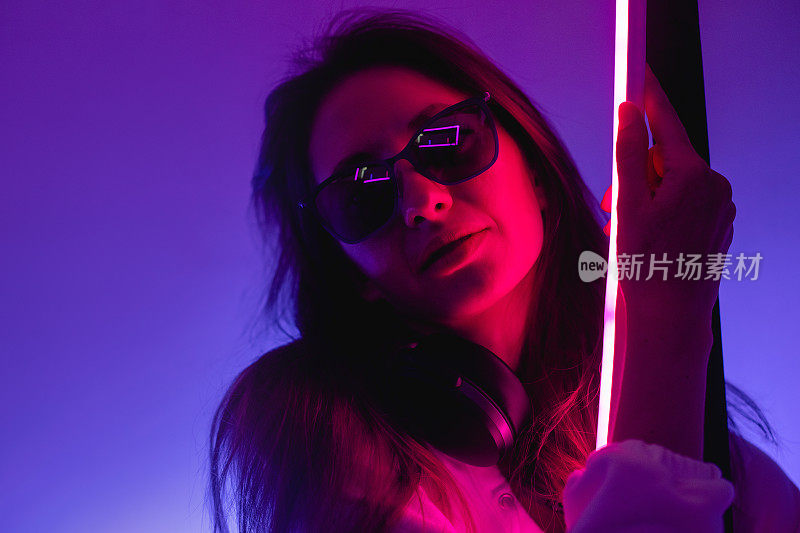 Female portrait in neon light. Fashion woman in purple color. Vibrant background at the studio. Futuristic concept. Girl wear sunglasses and hoodie with bluetooth wireless headphones